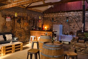 Un intérieur rustique avec un mur en pierre, des sièges en forme de tonneaux en bois, un coin bar et une cheminée.