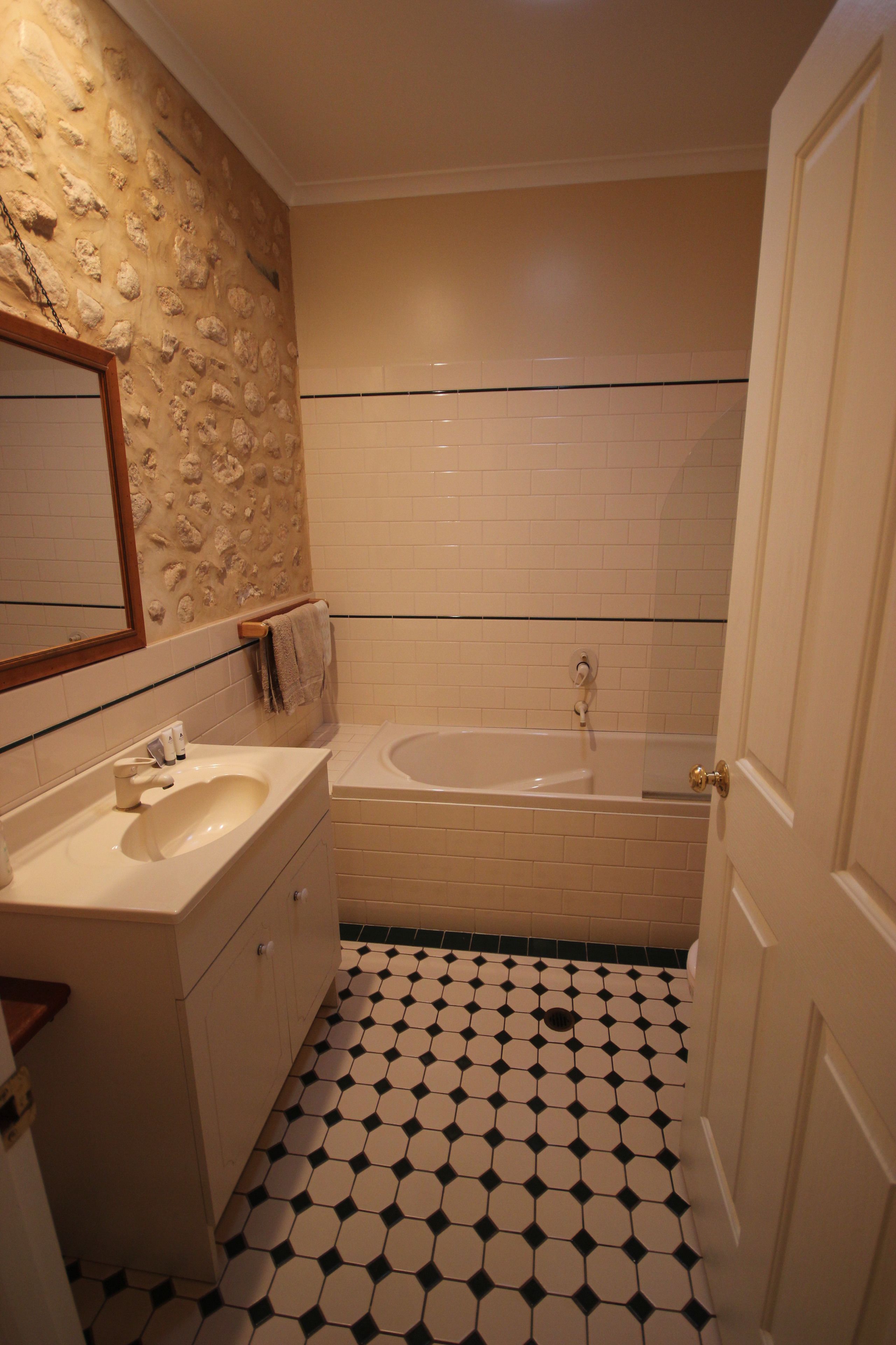 Une salle de bain avec un mur en pierre, un lavabo, une baignoire et un sol carrelé.