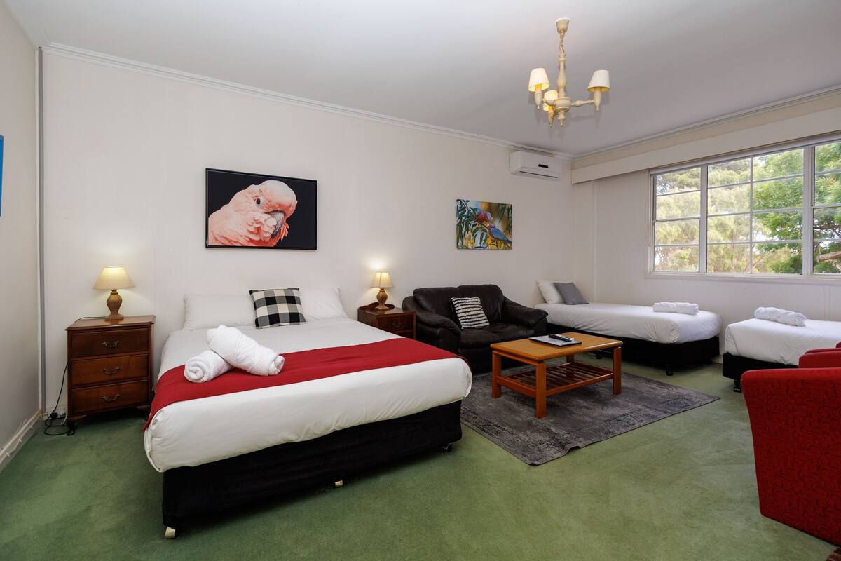 Une chambre d’hôtel avec un grand lit, deux petits lits, un canapé, une table basse et des œuvres d’art accrochées aux murs.