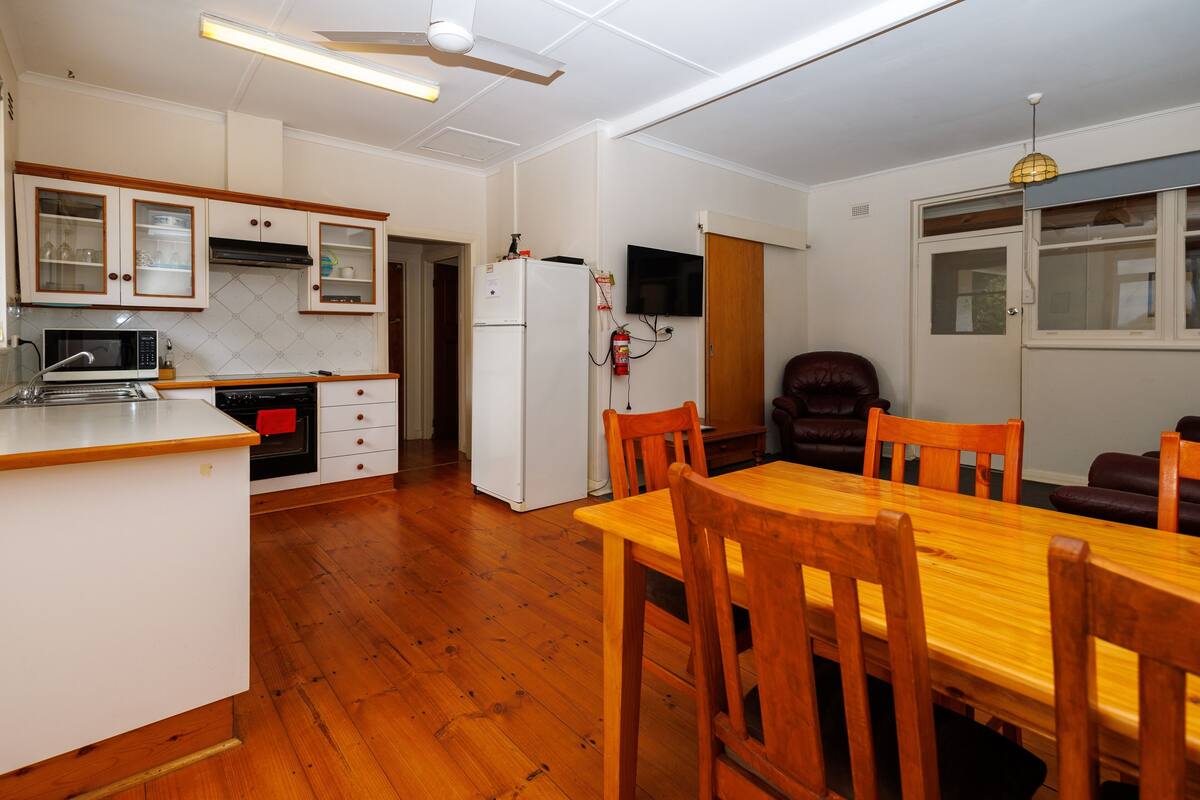 Une cuisine dotée de meubles en bois, d’un four à micro-ondes, d’un réfrigérateur et d’un coin repas avec une table et des chaises en bois.