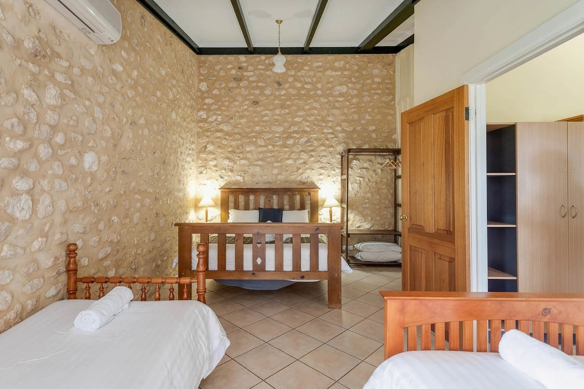 Une chambre avec deux lits, une armoire en bois et un mur décoré d’un motif imitant la pierre.