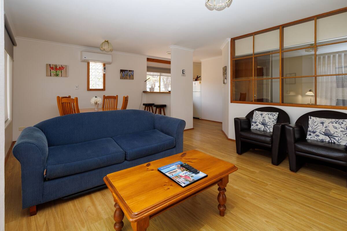 Un salon avec un canapé bleu, une table basse en bois et deux fauteuils en cuir noir.