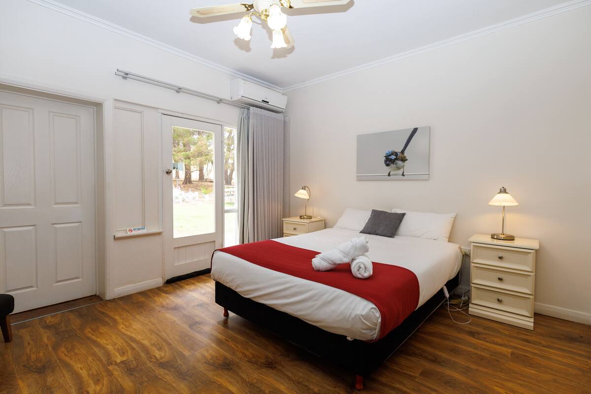 Une chambre à coucher bien rangée, avec un grand lit, deux tables de chevet et un ventilateur de plafond.