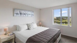Een slaapkamer met een groot bed, twee nachtkastjes, een raam met uitzicht op een stadsgezicht en een schilderij aan de muur.