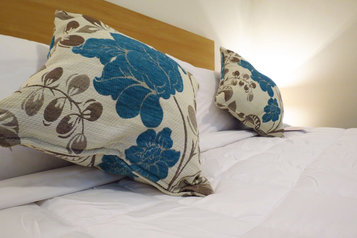 Una cama con sábanas blancas y dos almohadas decorativas con motivos florales.