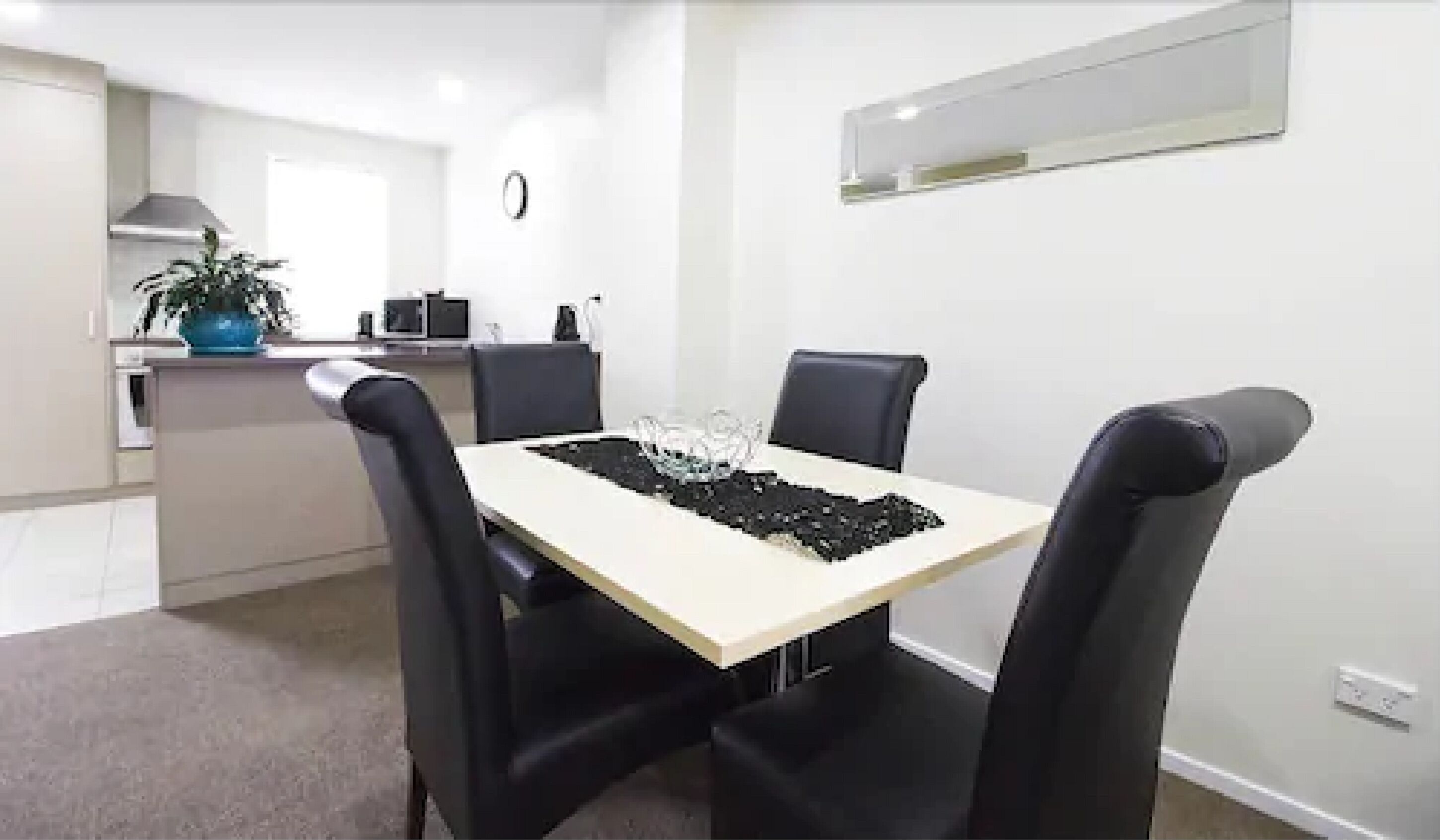 A modern dining area with a rectangular table, four black chairs, and a small potted plant on the counter.