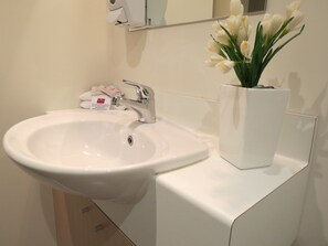 Un lavabo blanc amb un aixeta cromada, un vas de flors blanques i un dispensador de sabó a la superfície.