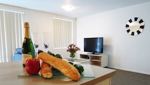 Een moderne woonkamer met een houten tafel, een fles champagne, glazen en een stokbrood. Er is een televisie op een dressoir en een klok aan de muur.