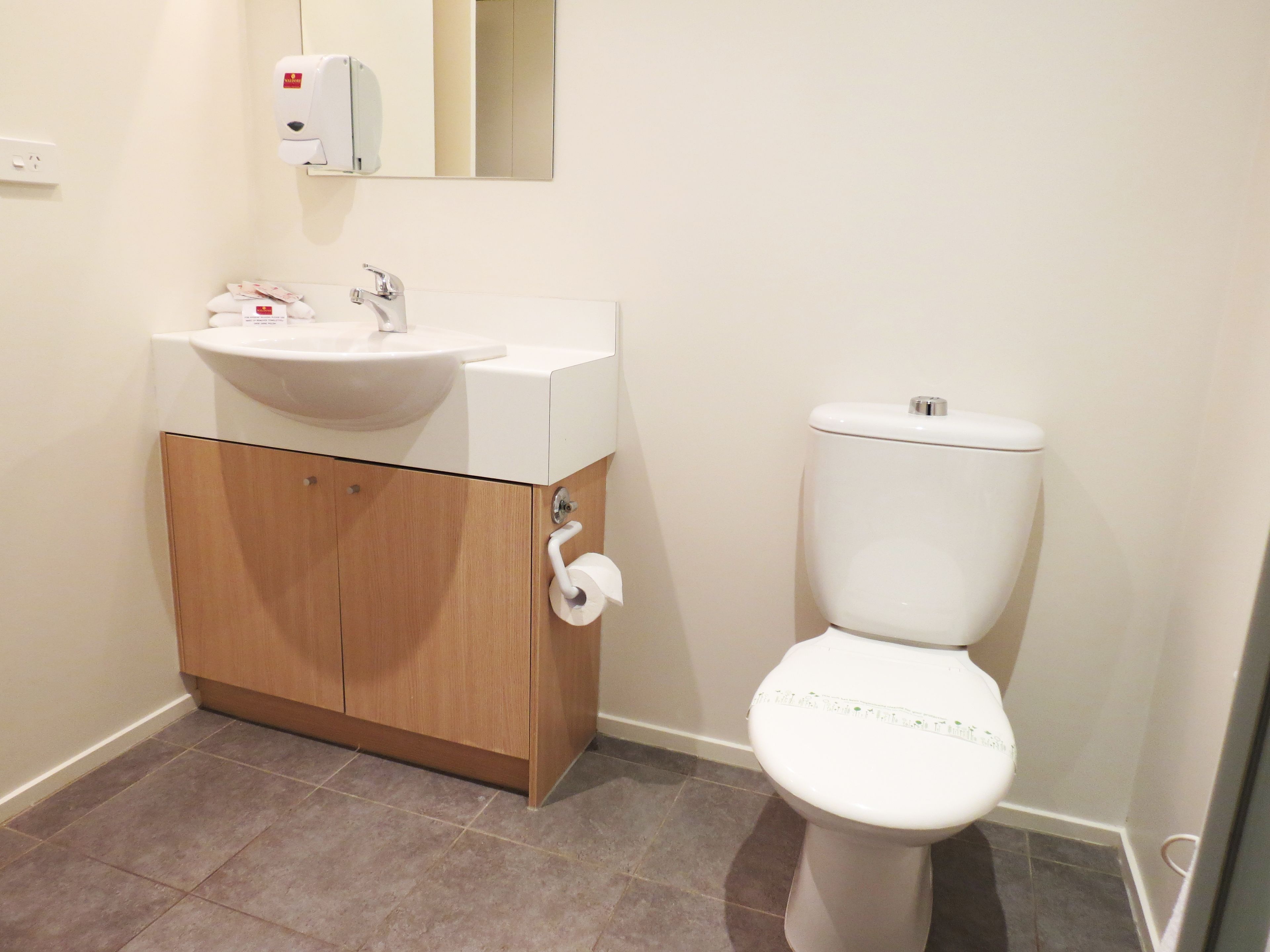 A bathroom with a white sink, toilet, and wooden cabinet.
