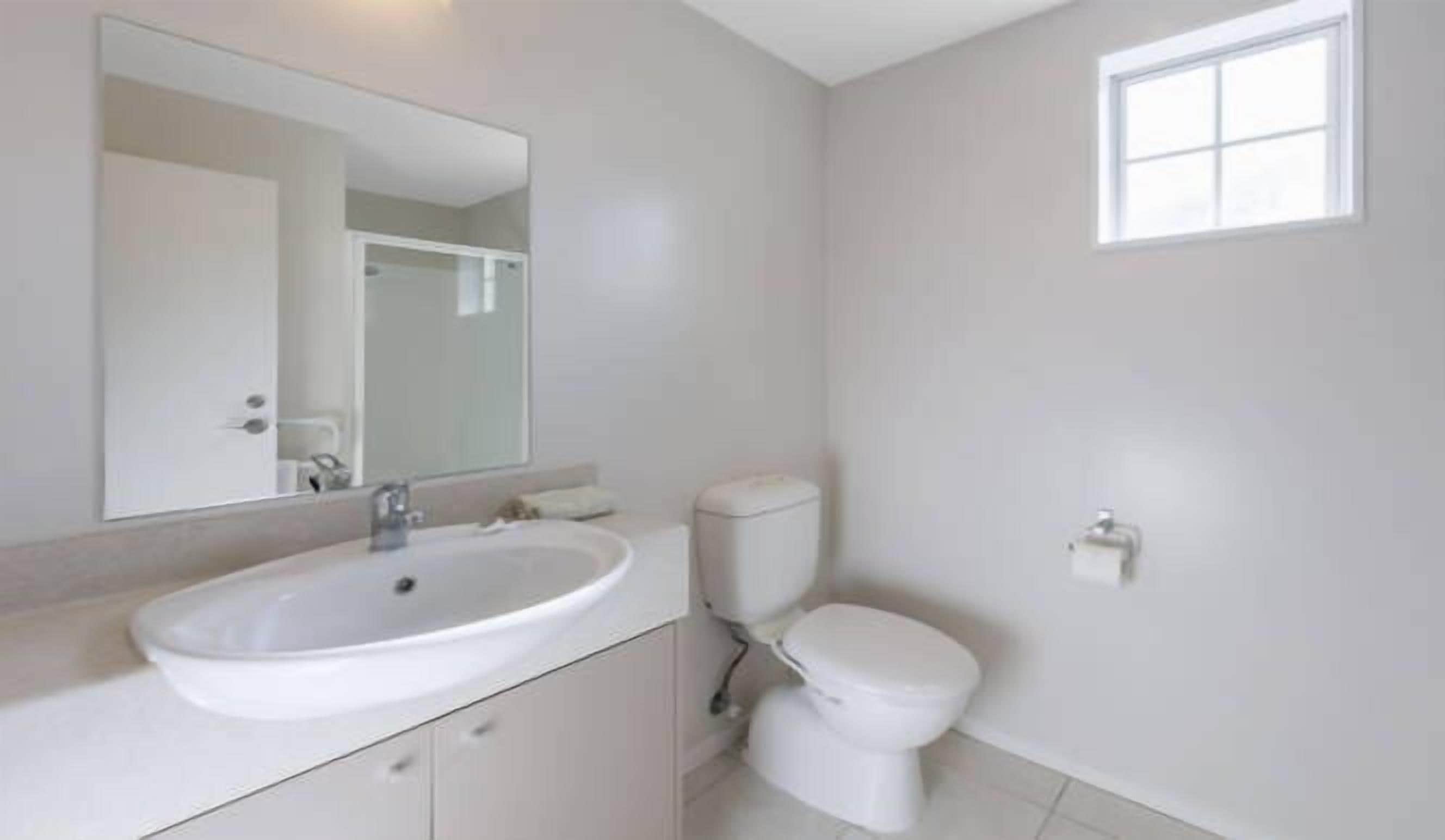 A bathroom with a white sink, toilet, and mirror.
