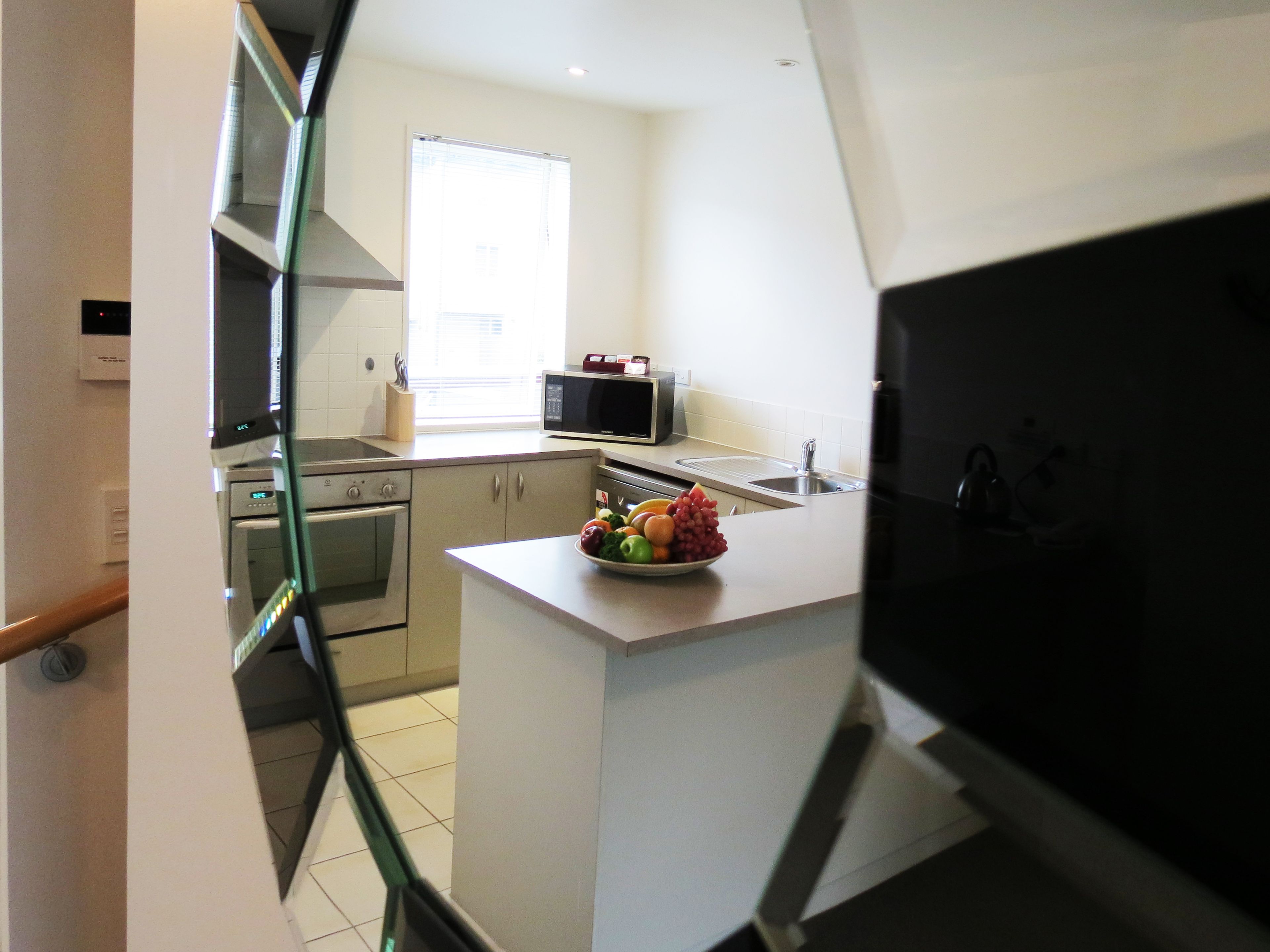 A compact kitchen with a microwave, stove, sink, and a bowl of fruit on the counter.