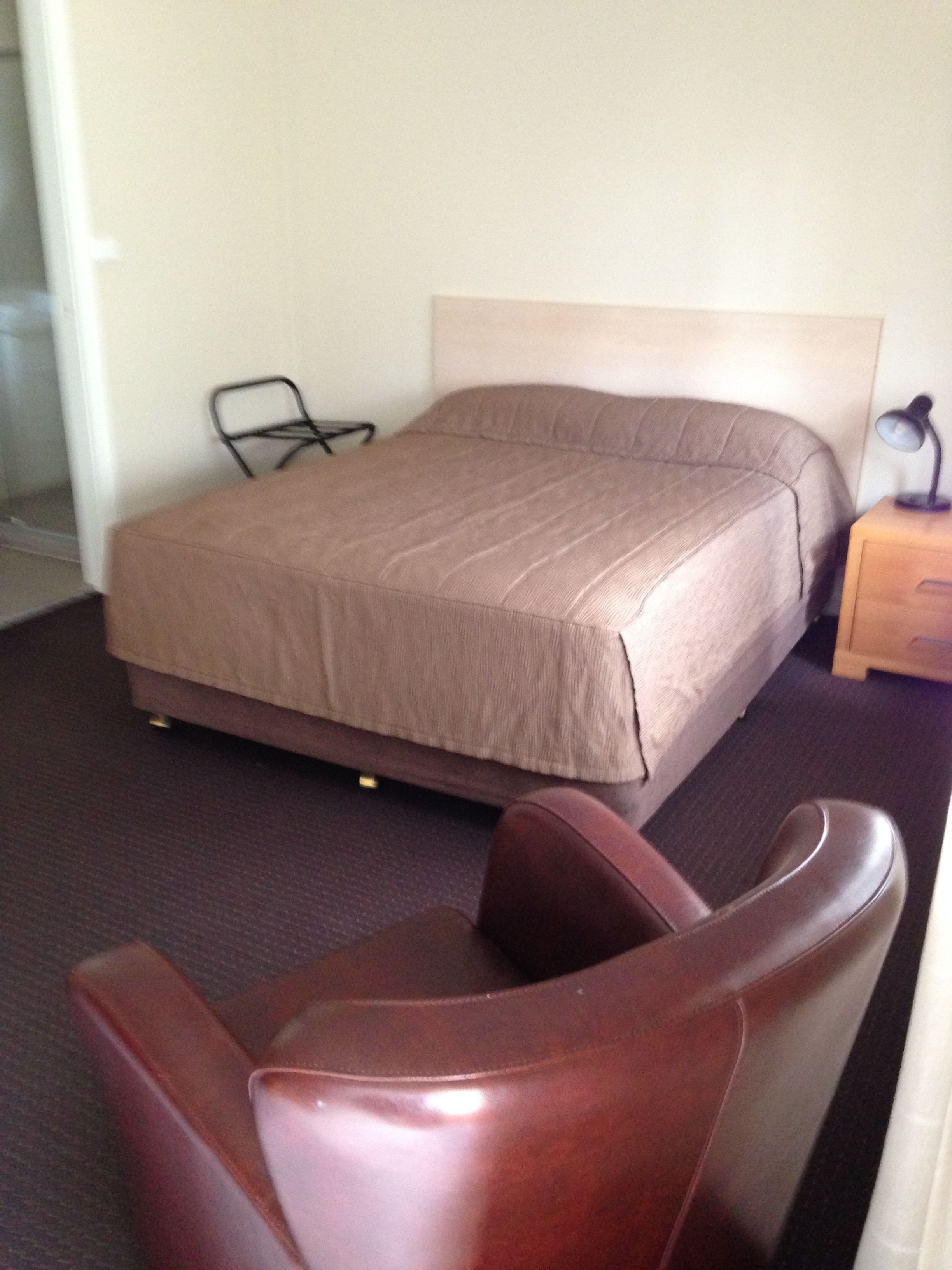 Quarto de hotel com cama, uma cadeira e mesa de cabeceira.
