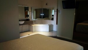 Una habitación de hotel con una cama grande, un baño con bañera, un lavabo y un espejo.