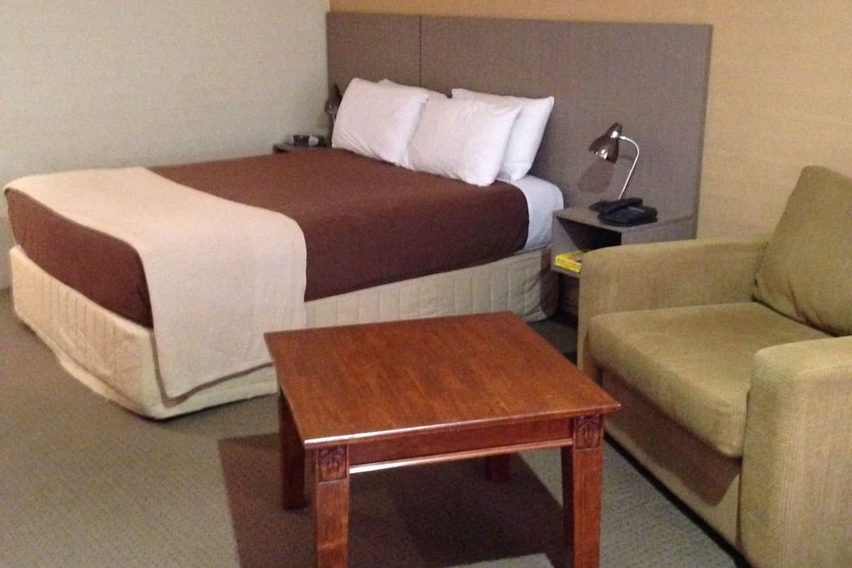 Una habitación de hotel con cama, mesita de noche, escritorio, silla y lámpara.