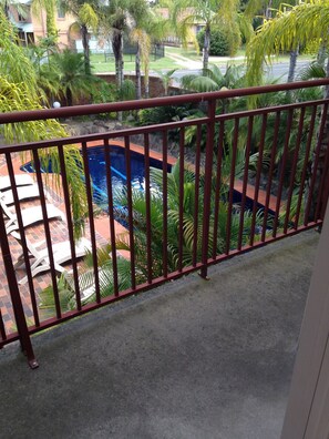 A pool area with a red metal railing, surrounded by palm trees and a brick pathway.