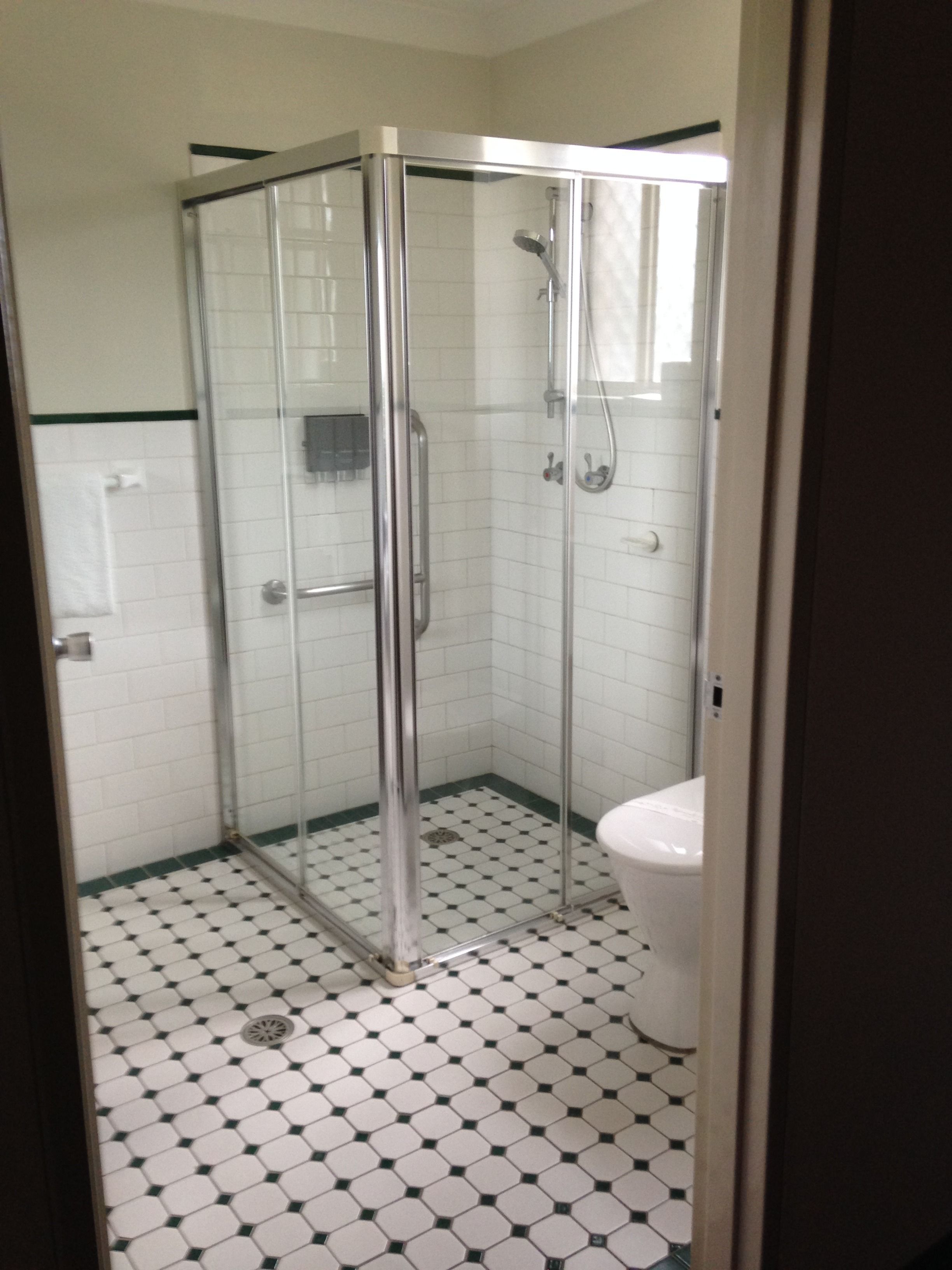 A bathroom with a glass shower enclosure, white toilet, and a tiled floor with a black and white pattern.