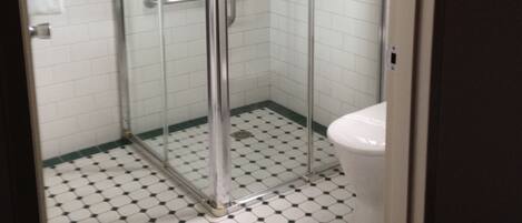 A bathroom with a glass shower enclosure, white toilet, and a tiled floor with a black and white pattern.