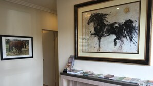 Un área de recepción con un cuadro enmarcado de caballos y una fotografía enmarcada de caballos, junto a un mostrador con folletos.