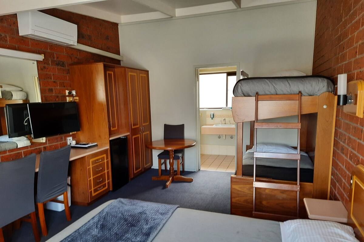Habitación de hotel compacta con literas, un escritorio con ordenador, televisor y baño pequeño.