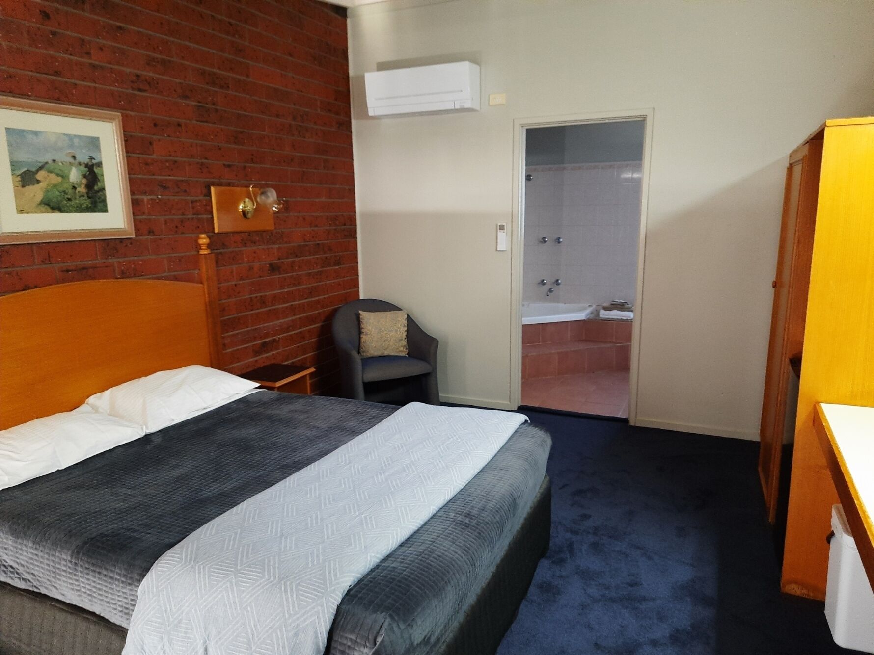A hotel room with a bed, a chair, a bathroom with a shower, and a wardrobe.