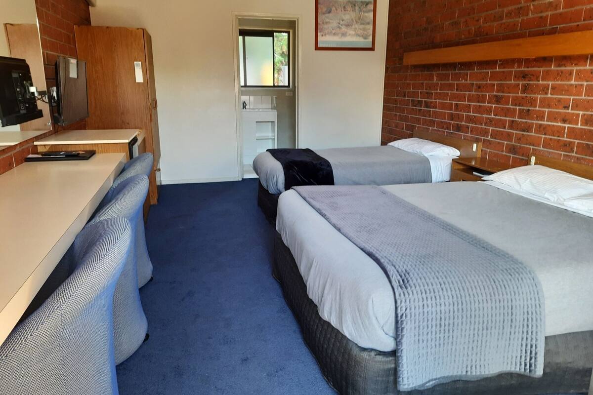 Habitación de hotel con dos camas, un escritorio, un televisor y una pared de ladrillo.