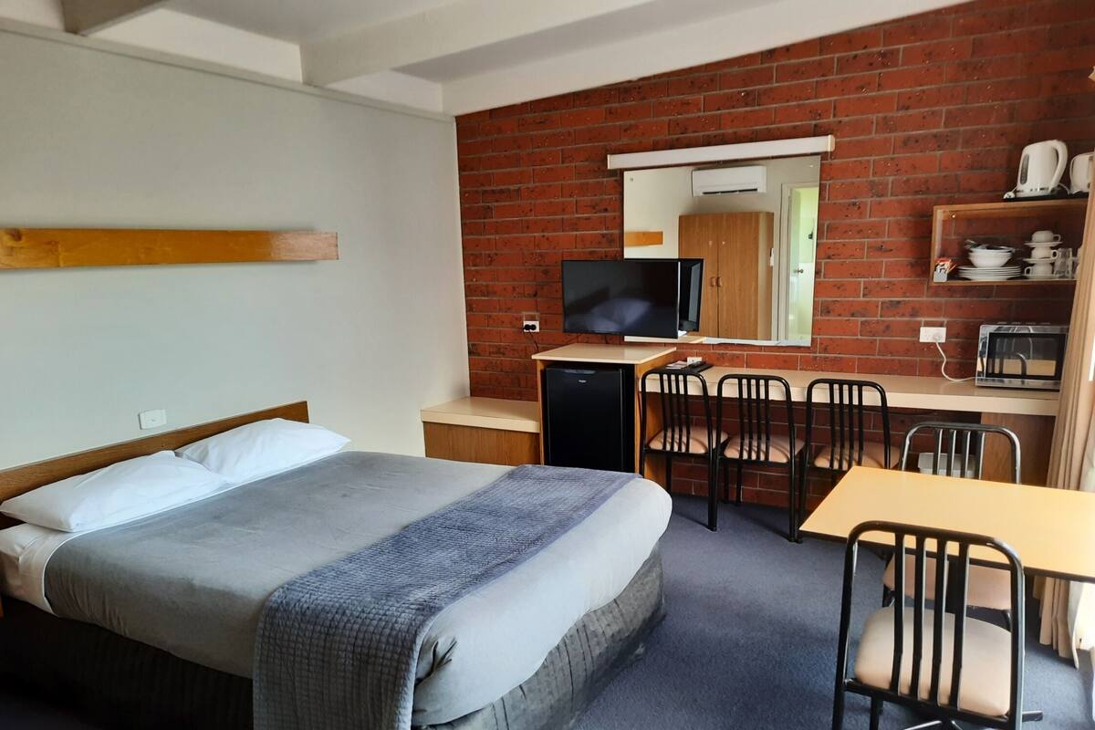 Una habitación de hotel con cama, escritorio, silla, televisor y pared de ladrillo.