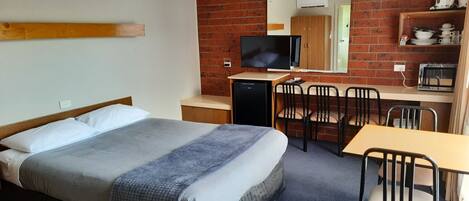 Una habitación de hotel con cama, escritorio, silla, televisor y pared de ladrillo.