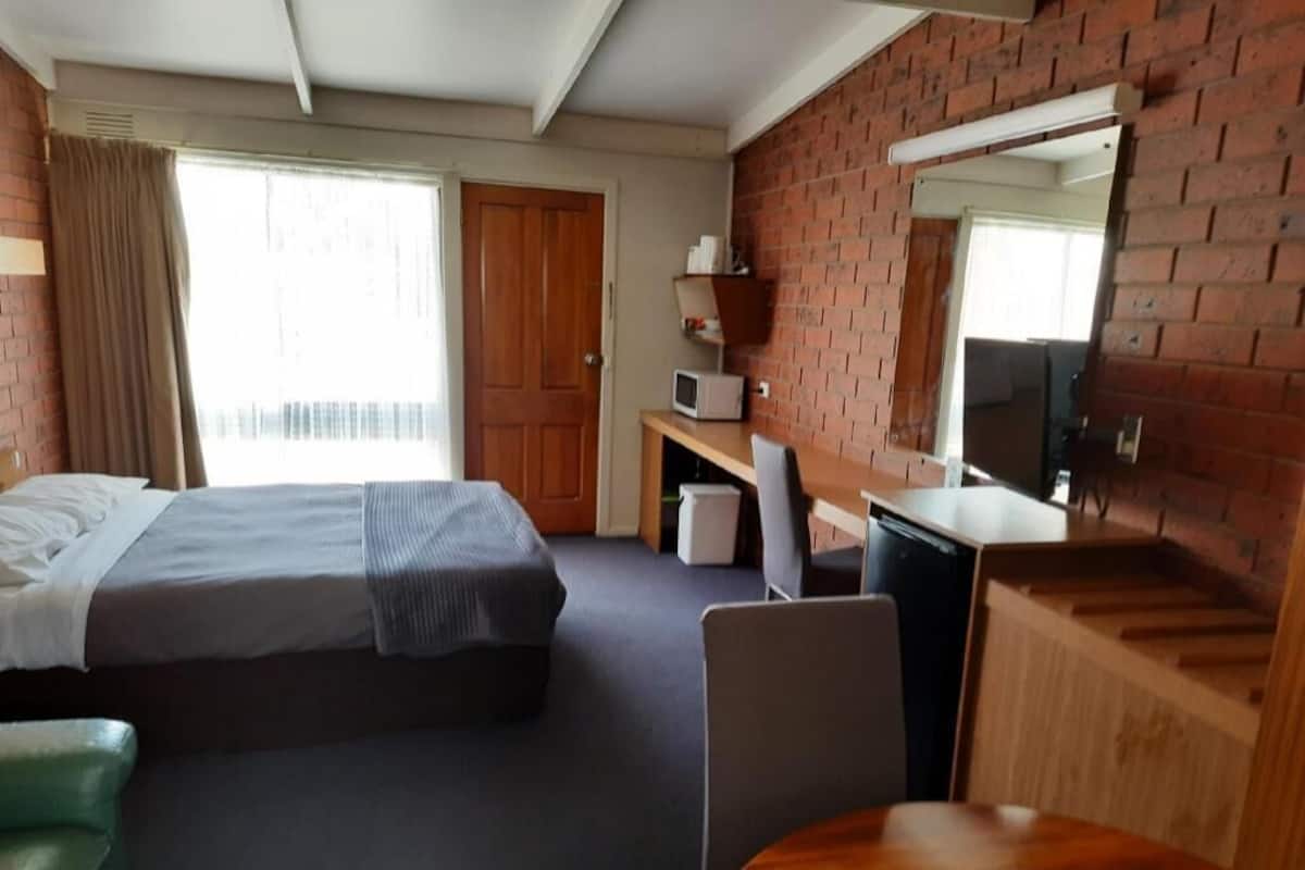 Habitación de hotel con cama, escritorio, silla, mesa, microondas y pared de ladrillo.