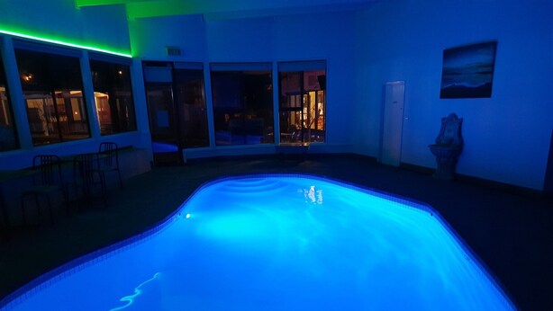 Une piscine éclairée de lumières bleues, une vue sur l’extérieur grâce à de grandes fenêtres et une statue ornant le mur.