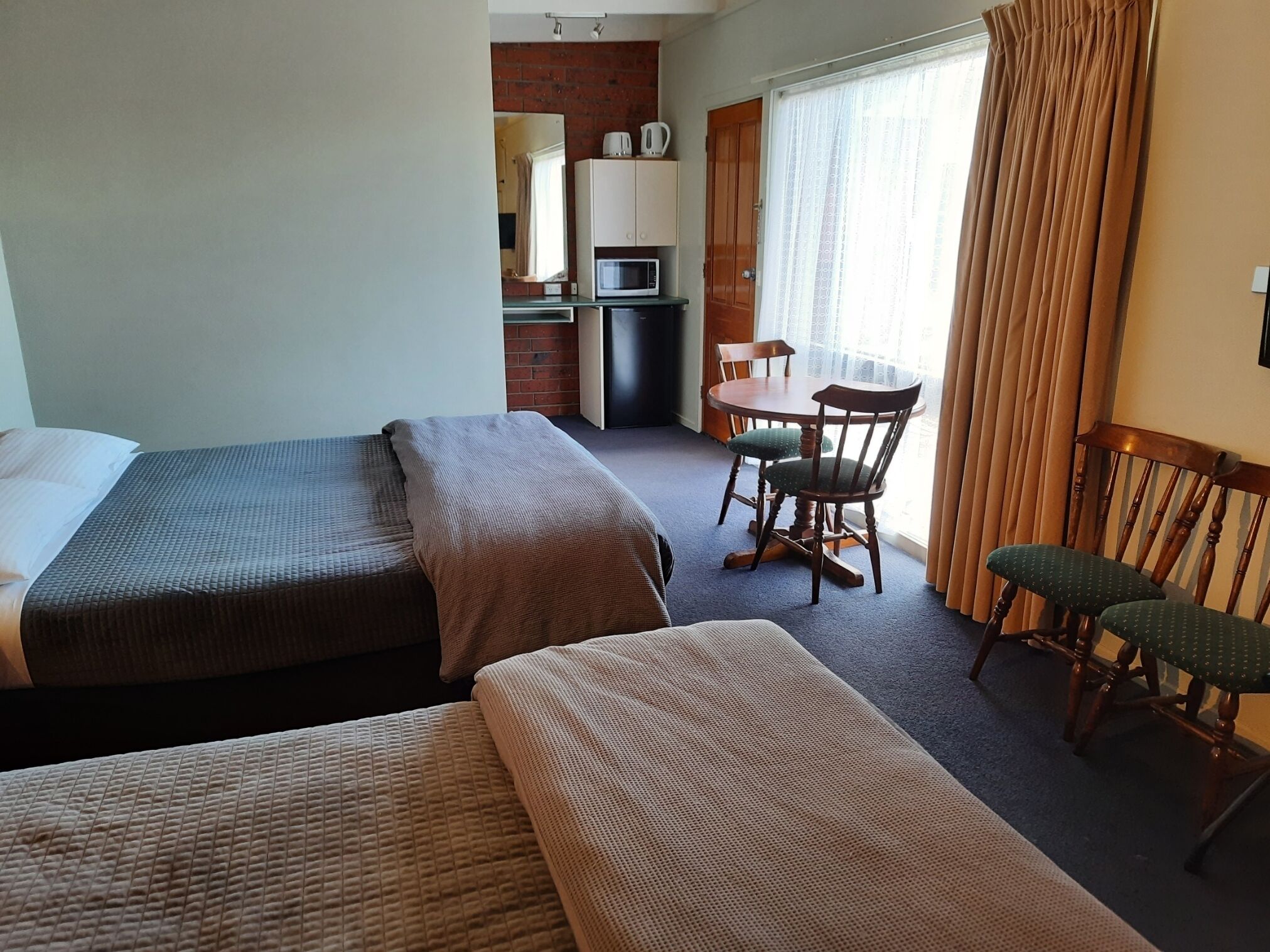 Habitación de hotel con dos camas individuales, una mesita con sillas, microondas y refrigerador.