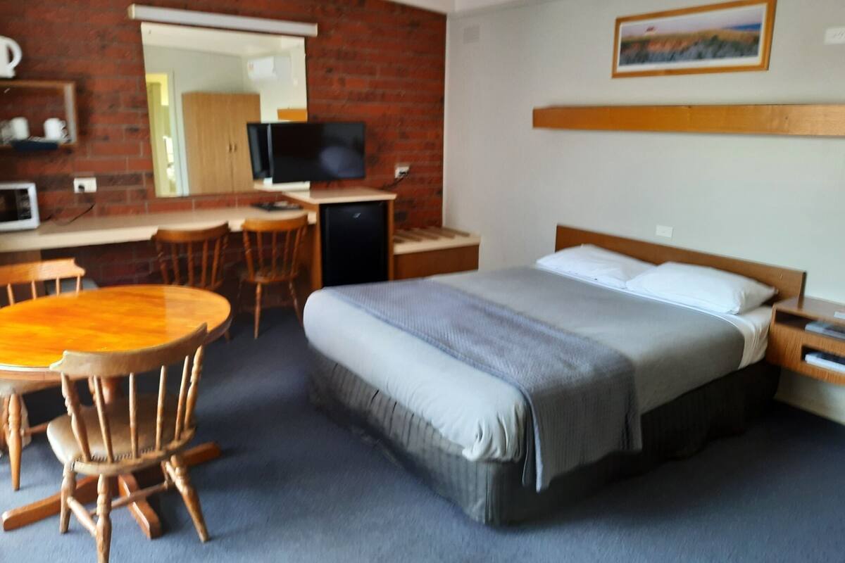Habitación de hotel con cama, escritorio, silla, televisión y una mesita.