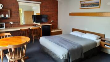 A hotel room with a bed, a desk, a chair, a television, and a small table.