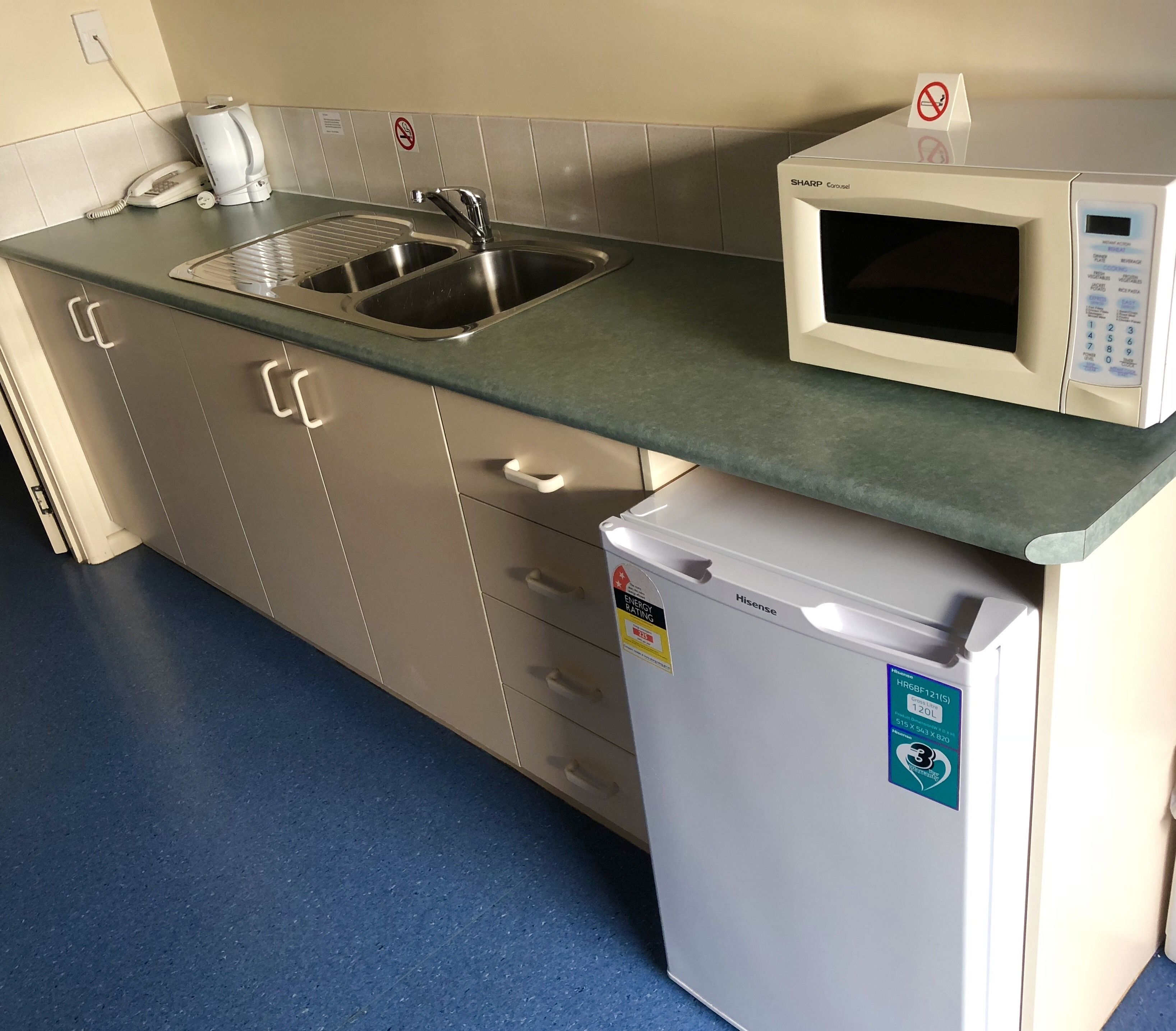 A kitchen with a stainless steel sink, a microwave, and a small refrigerator.