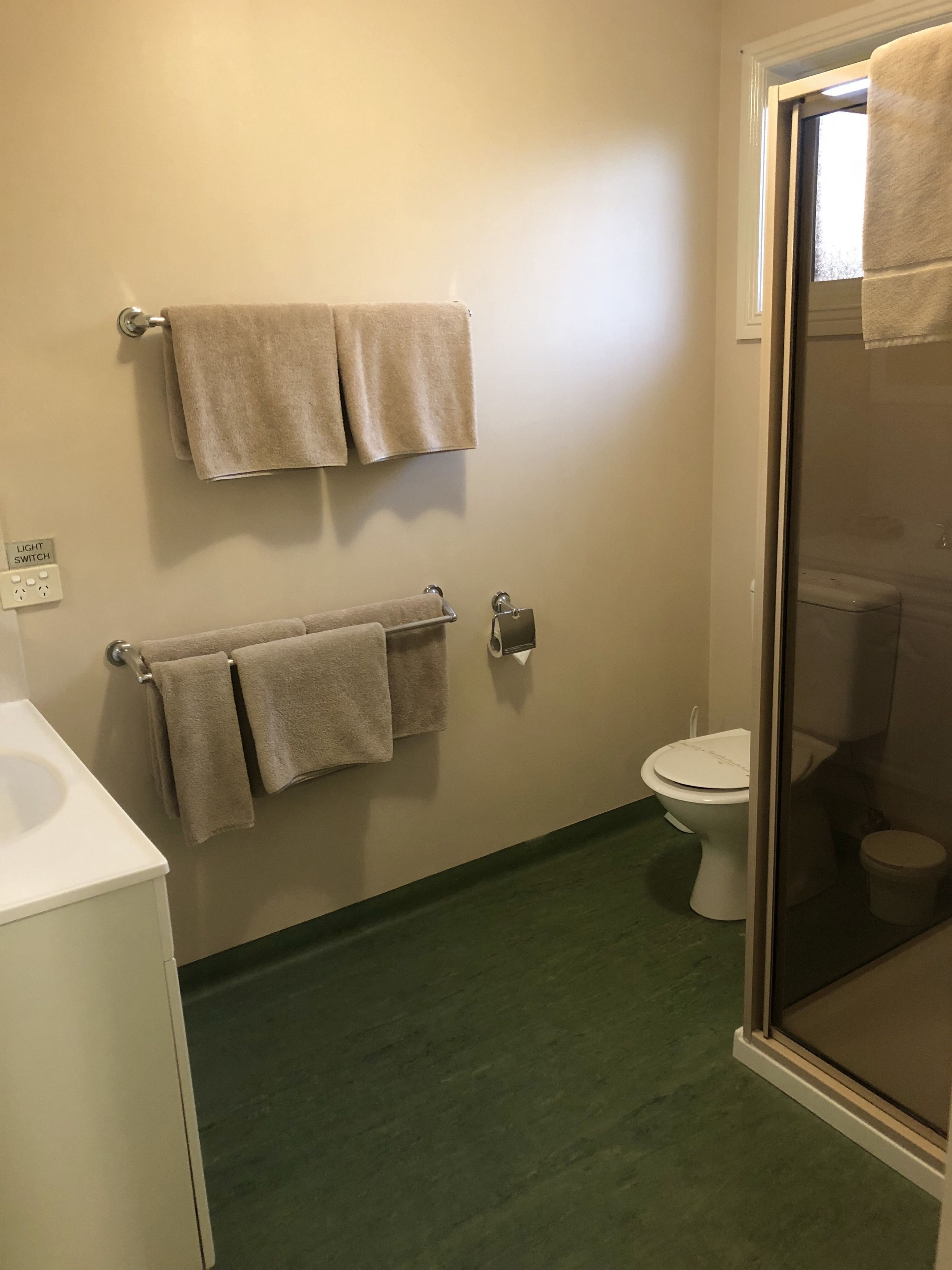 A bathroom with a toilet, a glass shower enclosure, and two towel racks with towels.