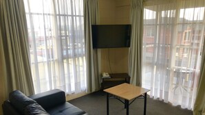 Uma sala de estar com um sofá de couro preto, uma mesa de centro de madeira e uma televisão de tela plana fixada na parede.
