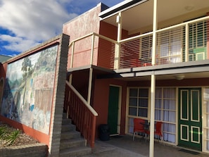 A two-story building with a balcony, a staircase, and a mural on the side.