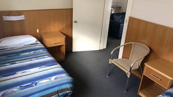 Habitación de hotel con dos camas, una silla, una mesita de noche y una puerta que da a otra habitación.