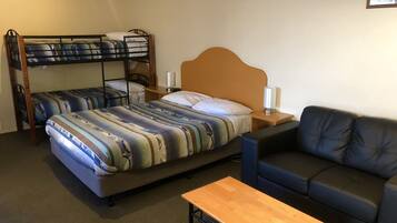 Habitación de hotel con una cama litera, un sofá, una mesa de madera y una mesita de noche con lámpara.