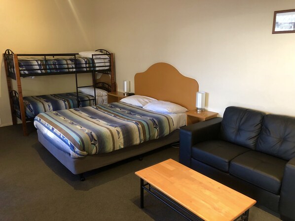 Habitación de hotel con una cama litera, un sofá, una mesa de madera y una mesita de noche con lámpara.