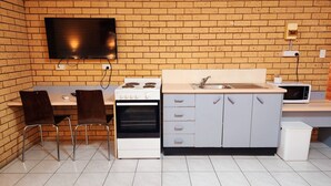 Cocina compacta con pared de ladrillo, televisión de pantalla plana, estufa, lavamanos y microondas.