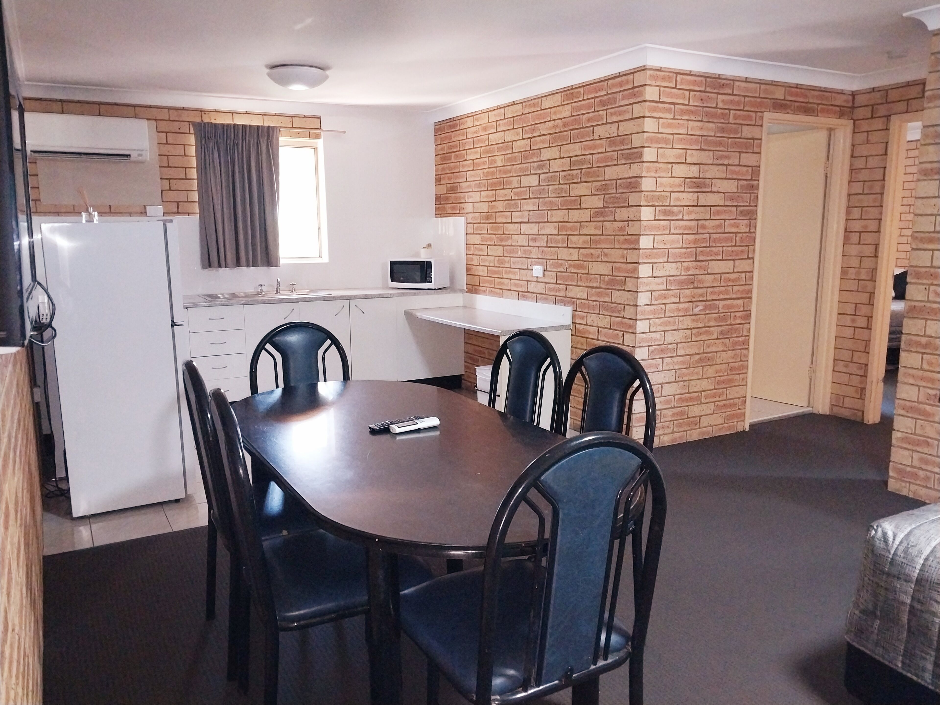 A compact room with a dining table, four chairs, a microwave, a refrigerator, and a brick accent wall.