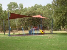 Un parque infantil con tobogán y columpio, rodeado de césped y árboles.
