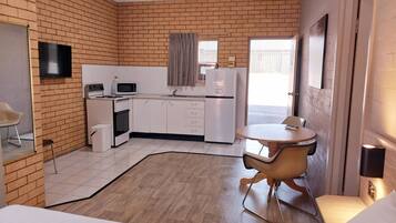 A compact hotel room with a kitchenette, a dining area, and a bed.