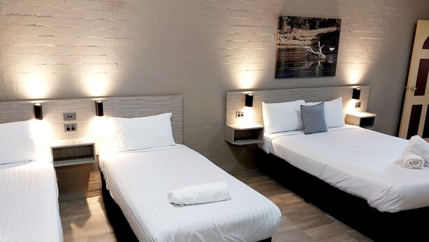 Habitación de hotel con dos camas individuales, cada una con una mesita de noche, una lámpara de pared y un enchufe.