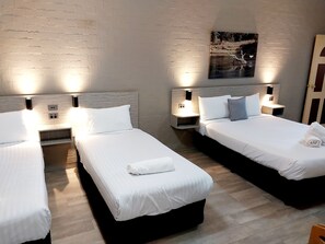 Habitación de hotel con dos camas individuales, cada una con una mesita de noche, una lámpara de pared y un enchufe.