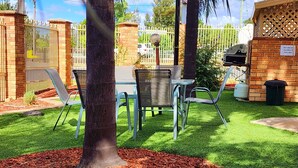 Un patio con mesa y sillas, rodeado por un muro de ladrillo y una cerca de metal.