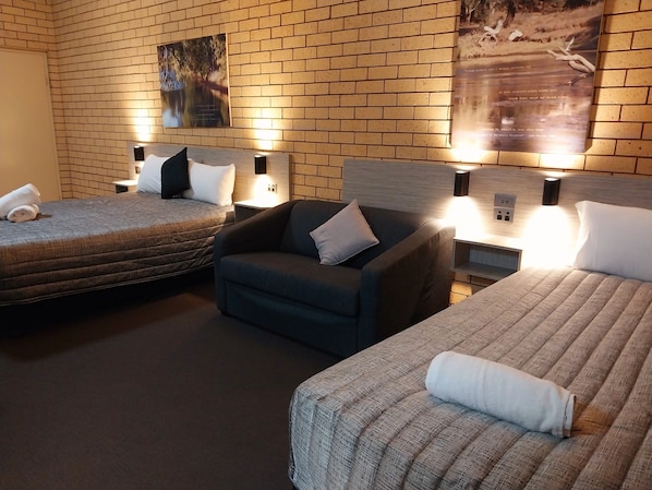 Habitación de hotel con dos camas, un sofá y una pared de ladrillo.