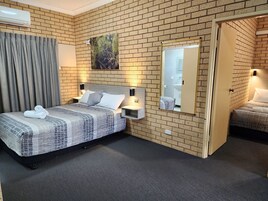 Camera d'albergo con parete in mattoni, un letto grande con copriletto fantasia grigio e bianco, due comodini con lampade, uno specchio grande e vista sul bagno.