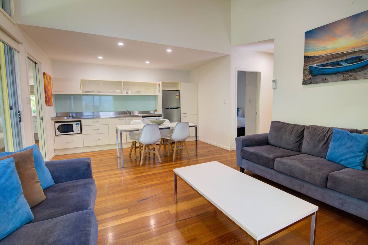 A modern living room with a grey sofa, a white coffee table, and a dining area with a white table and chairs.