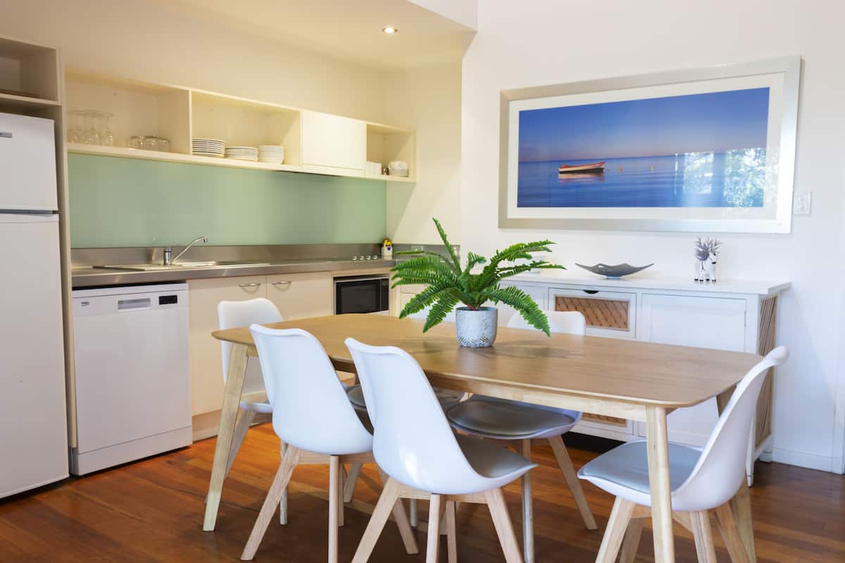 A modern kitchen with white cabinets, a wooden dining table, and four white chairs.